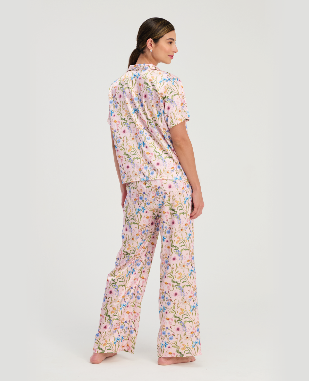 Mujer de espalda vistiendo pijama St. Even en satín rosa con estampado floral, camisa manga corta y pantalón largo.