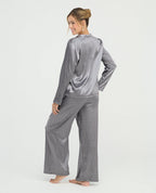 Mujer usando pijama de satín gris de pantalón y camisa manga larga, vista posterior con textura brillante y suave.