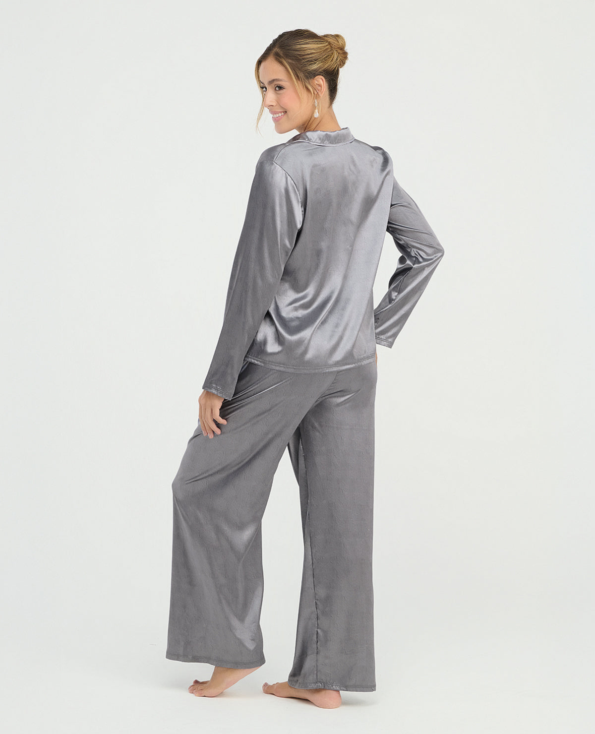 Mujer usando pijama de satín gris de pantalón y camisa manga larga, vista posterior con textura brillante y suave.