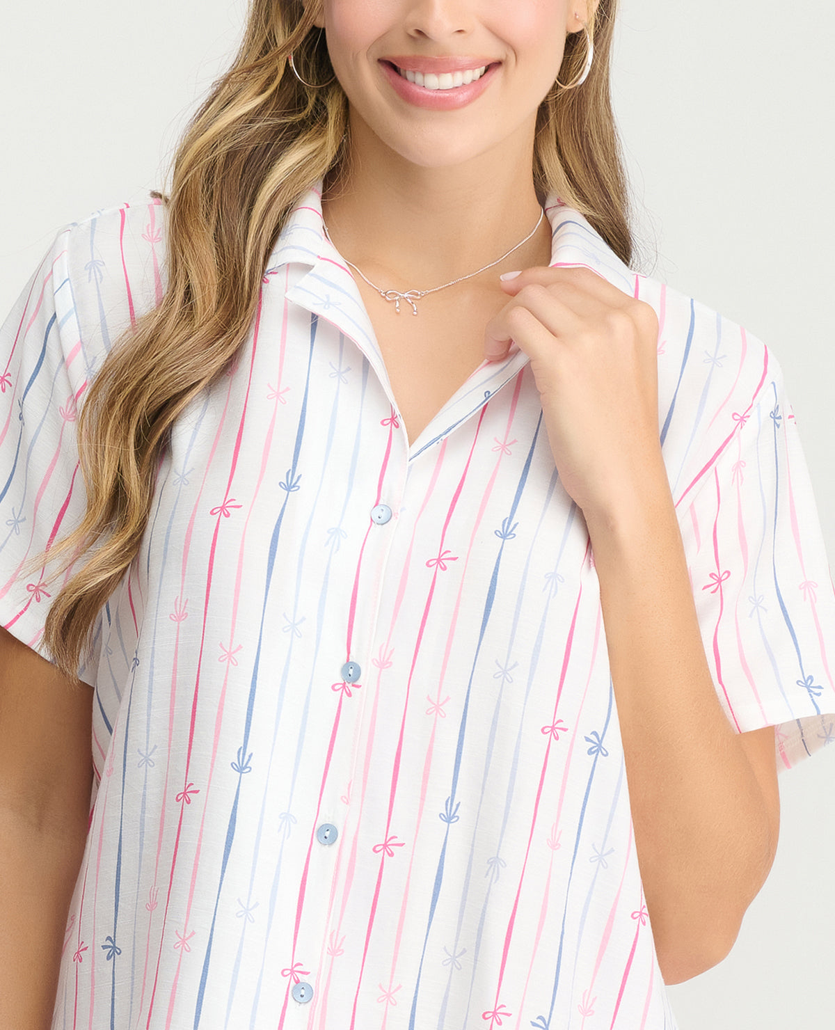 Primer plano de camisa de pijama para mujer manga corta blanca con rayas rosadas y azules y botones frontales.