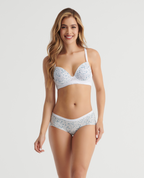 Modelo luciendo brasier de realce medio con estampado azul, copas lisas y base de encaje blanco con cargaderas ajustables.