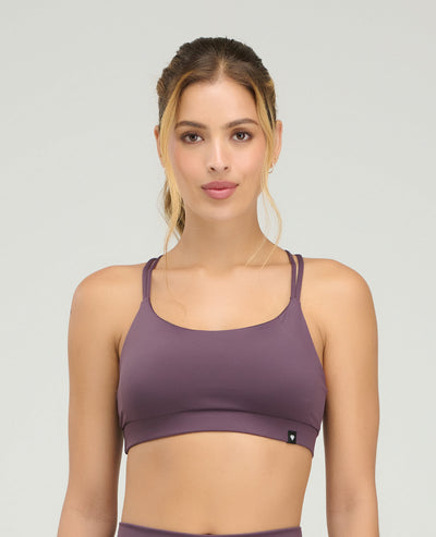 Mujer usando top deportivo morado de silueta ajustada con copas suaves y cargaderas dobles sobre fondo gris.