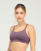 Top deportivo color morado para mujer con copas fijas suaves y cargaderas dobles sobre fondo gris claro.