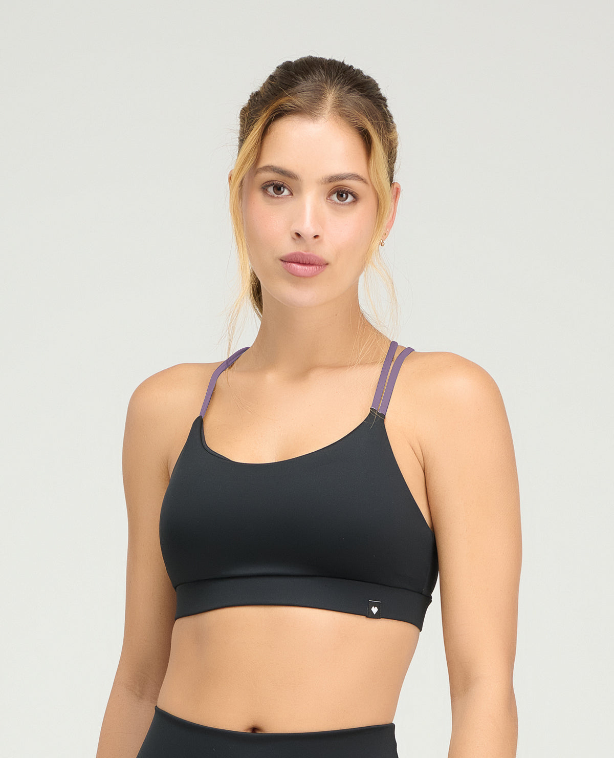 Top deportivo negro para mujer con copas fijas suaves y cargaderas dobles moradas en contraste.