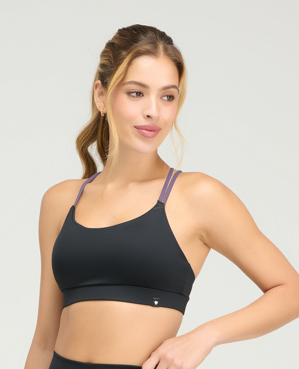 Top deportivo negro con copas fijas suaves y cargaderas dobles lilas en diseño de espalda cruzada.