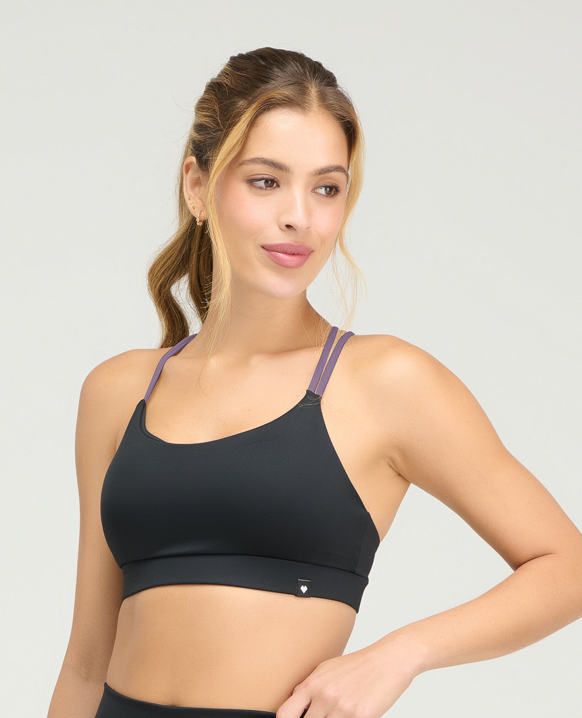 Top deportivo negro con copas fijas suaves y cargaderas dobles lilas en diseño de espalda cruzada.