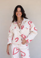 Ivory cotton drill denim jacket with all-over red heart print, front pockets, and barrel sleeves