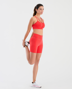 Mujer usando short deportivo tipo ciclista talle alto y largo medio en color rojo con detalles en gel laterales.