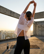 Mujer estirando en azotea al atardecer con la Camiseta Deportiva Cropped Transpirable St.Even de malla blanca con abertura.