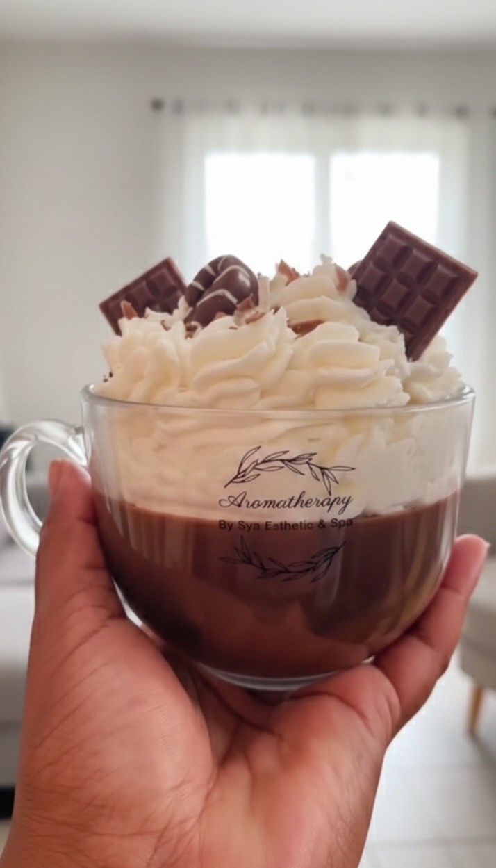 Hand holding a glass of hot chocolate with whipped cream and chocolate pieces, blurred indoor background