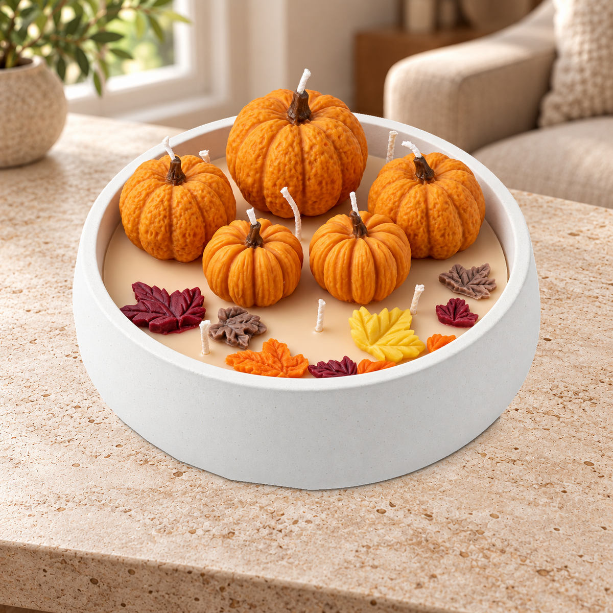 Vela Pumpkin Harvest de Sya apagada, con calabazas naranjas y hojas de cera en una fuente blanca apoyada sobre una mesa de piedra.